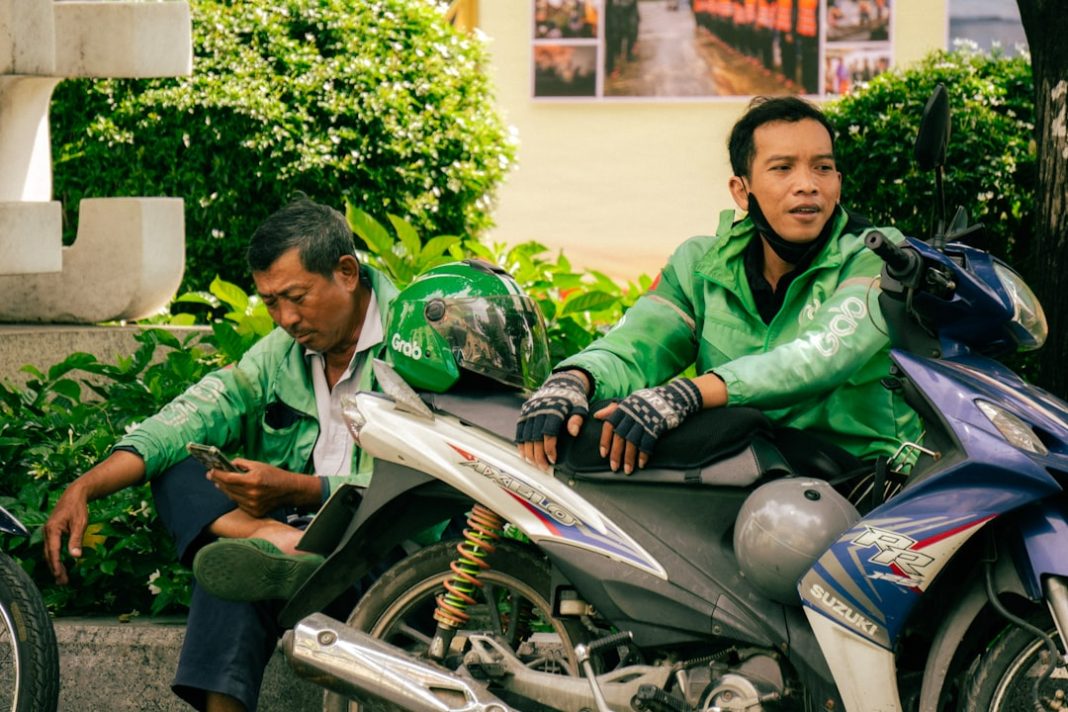 Two men in green jackets sit on motorcycles.